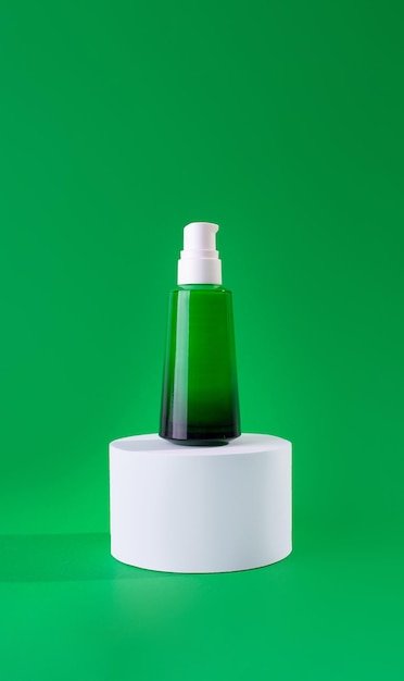 Green glass bottle of cream or serum on a stand white podium on green background Design Template