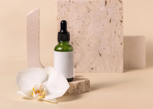 Green glass dropper bottle near white orchid flower on light yellow Mockup Skincare product