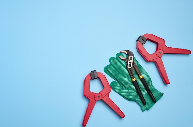 Green glove and metal universal adjustable wrench on a blue background top view