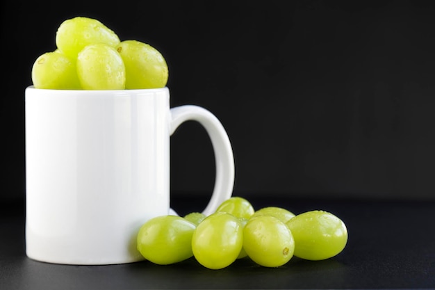 Green grapes portion inside a white mug on black background with copy spacexAxA