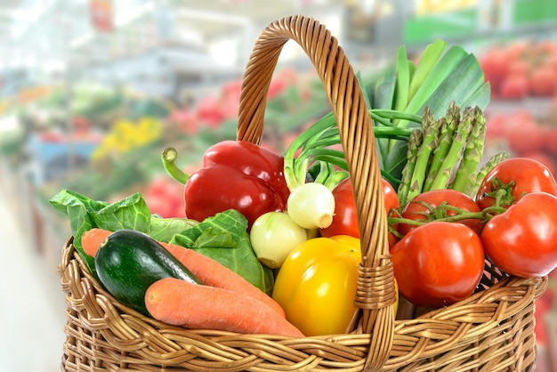 Green Grocery shopping concept image basket full of varied fresh vegetables on a blurred supermarket background