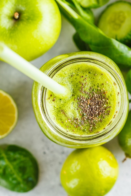 Green healthy smoothie (juice) in the jar, top view. Apple, spinach, cucumber smoothie on white surface with the ingredients.