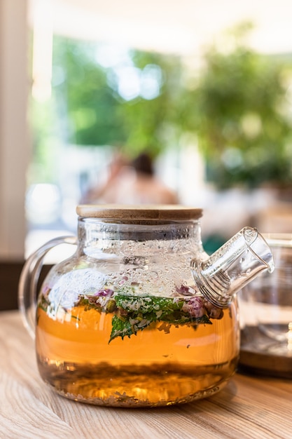 green or herbal tea in glass teapot with mint and roses petals blurred background