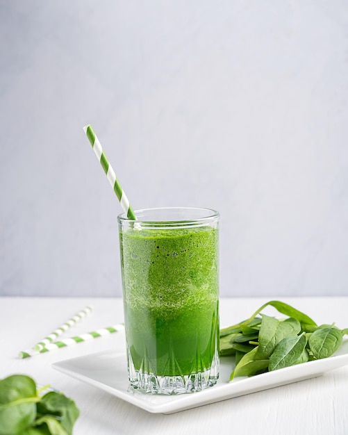 Green homemade vegetarian smoothie or juice made of spinach leaves served on white wooden table