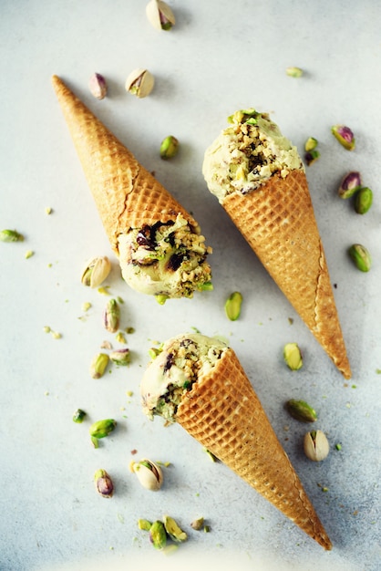 Green ice cream in waffle cone with chocolate and pistachio nuts on grey stone . Summer food concept, copy space. Healthy gluten free ice-cream.