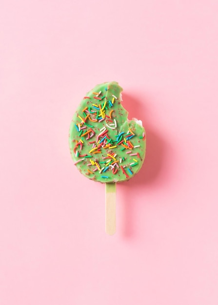 Green ice cream with sprinkle on stick on pink background flat lay