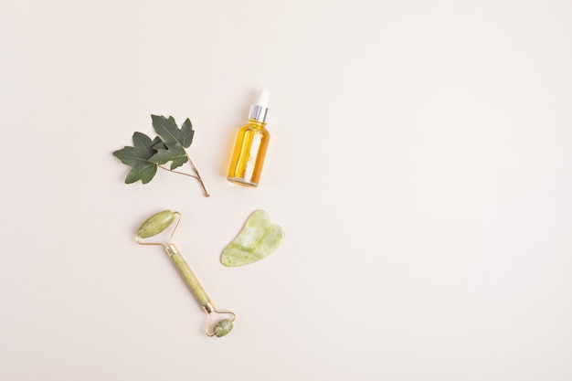 Green jade face roller, gua sha stone, essential oil. Natural skin care concept. Top view, flat lay