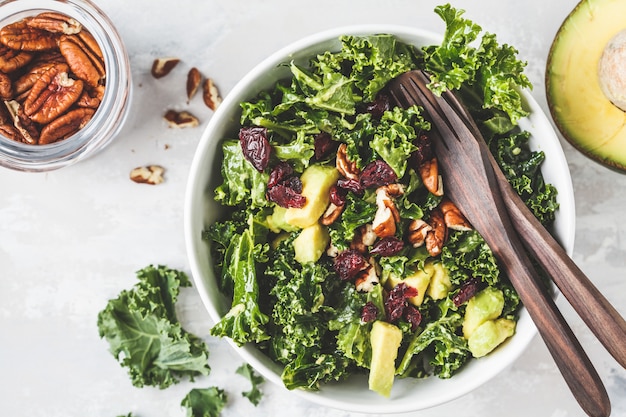 Green kale salad with cranberries and avocado in white bowl, top view. Healthy vegan food concept.