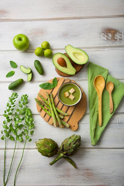 Green kitchen utensils and vegetables on wooden floor avocado artichokes