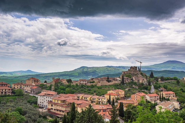 Green landscape in Tuscany Italy Unique view of medieval village and stone tower perched on rock cliff against dramatic sky