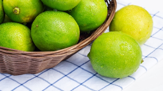 Green lime in a basket on a white wooden table.