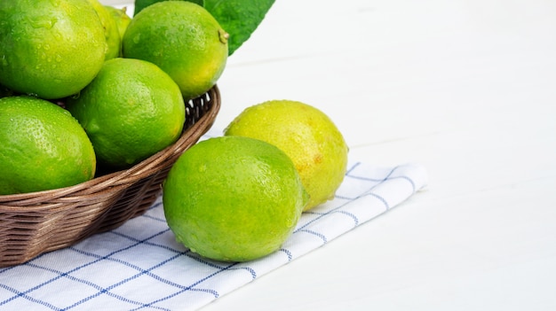 Green lime in a basket on a white wooden table.