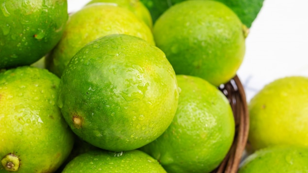 Green lime in a basket on a white wooden table.