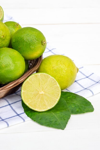 Green lime in a basket on a white wooden table.