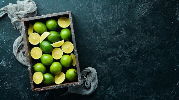 Green lime in a wooden box Citrus fruits On a black stone background Top view Free space for your text