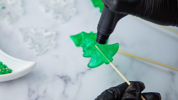 A green lollipop in the form of a christmas tree is held in the hands of black gloves and burned on