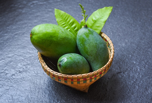 Green Mango summer fruit and green leaves in the basket on dark