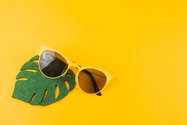 Green monstera leaf with sunglasses on yellow background