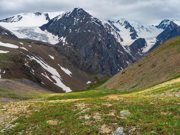 Green mountain slope, a view of a deep mountain valley with stunning snow peaks in the background.