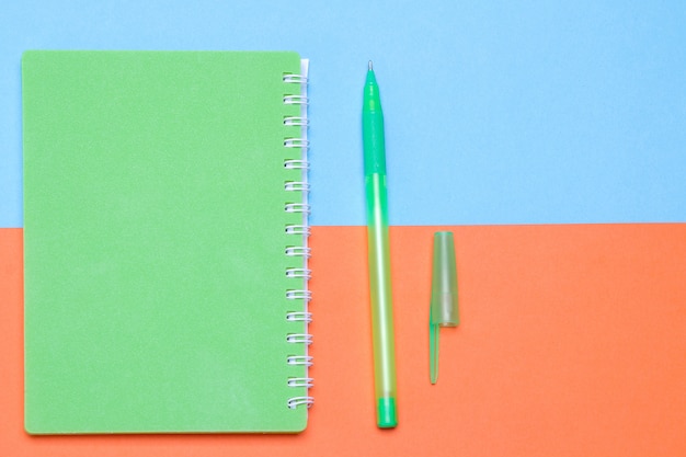 Green notebook with a pen on a  multi-colored background.