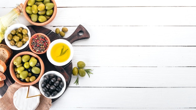 Green olives and black olives oil bread cheese and snacks Italian cuisine On a white wooden table Top view Free space for text