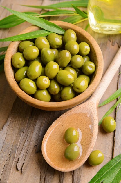 Green olives in bowl with leaves on table closeup