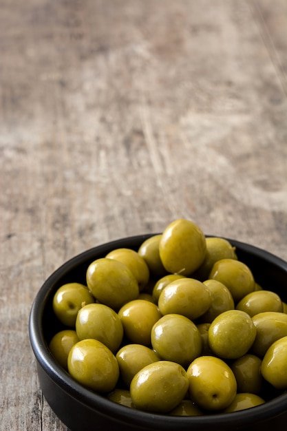 Photo green olives in bowl on wooden table copy space