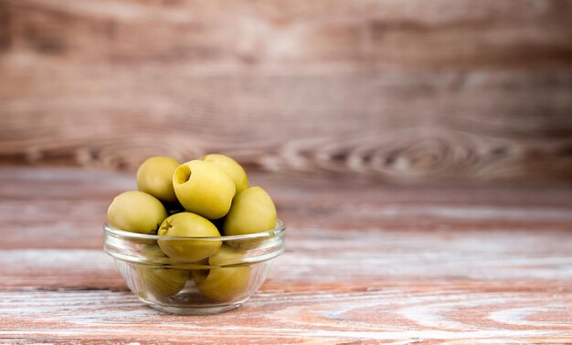 Green olives in a glass bowl on wooden background Closeup Copy space