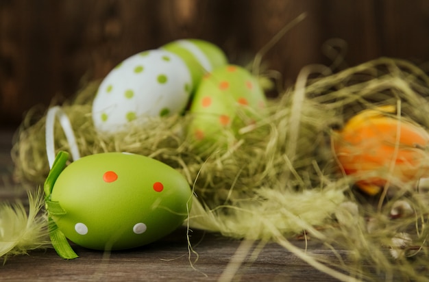 Green and orange easter eggs in a sisal nest on a wooden surface copy space. Painted eggs. Bird feathers