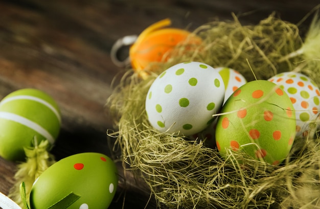 Green and orange easter eggs in a sisal nest on a wooden surface copy space. Painted eggs