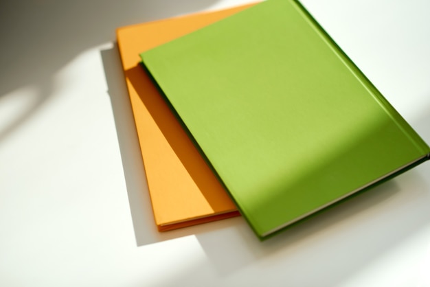 Green and orange notepads lie under the sun on the table . High quality photo