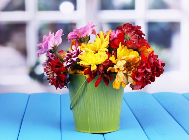 Green pail with flowers on blue wooden table on window background