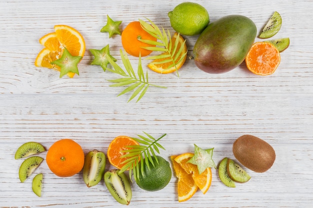 Green palm leaves and fresh tropical slices of fruits on white wooden table