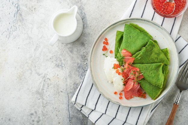 Green pancakes Round thin green spinach crepe pancakes with red and black caviar and yogurt sauce on gray concrete background Healthy vegan breakfast National Pancake Day or Fat Tuesday Day