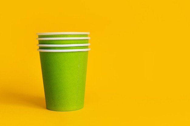 Green paper cups stack on yellow background Ecofriendly concept biodegradable disposable tableware