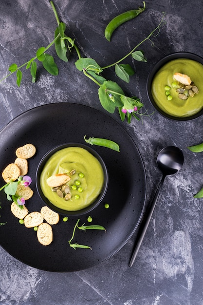 Green peas cream soup with croutons in a black bowl