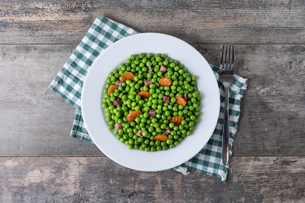 Photo green peas with serrano ham and carrot on wooden table