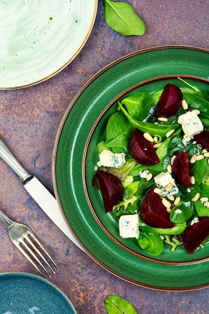 A green plate with spinach salad on it and a fork on the side.