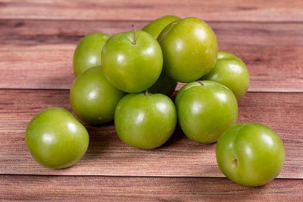 Green plum on wood background Pile of green plums close up