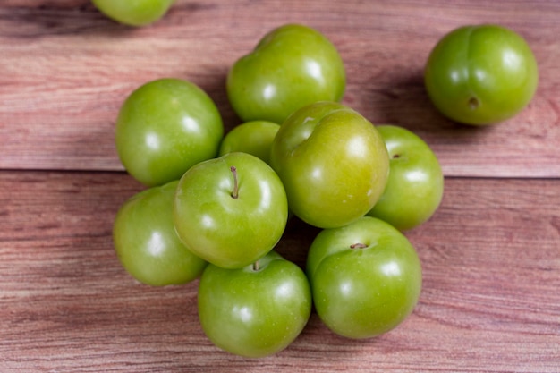 Green plum on wood background Pile of green plums close up