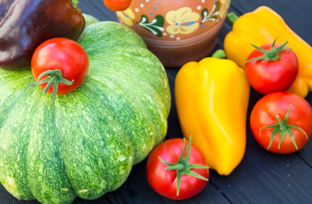 Green pumpkin, tomatoes, pepper and jug on a black wooden background