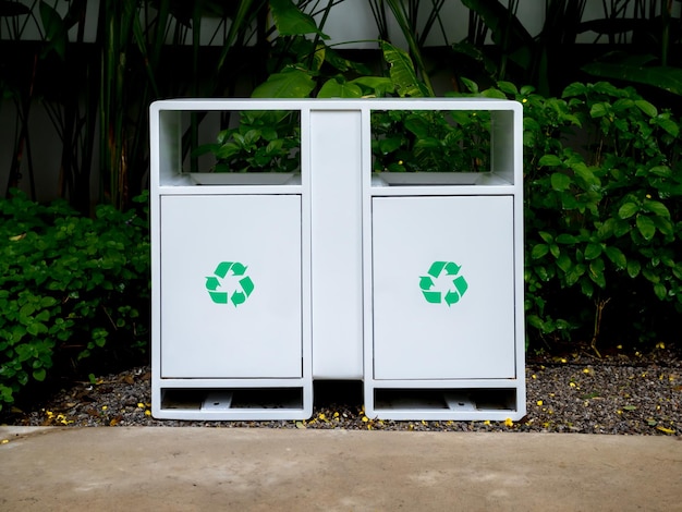 Green recycle icon symbols on modern white twin iron rectangle recycle bins in the green garden in front of the building beside the concrete walkway