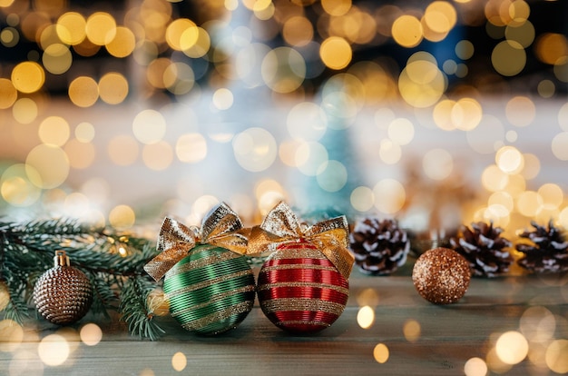 Green and red Christmas bulbs with golden bows, fir tree branches and ornaments on wooden background with Christmas lights bokeh, Merry Christmas greeting card with copy space