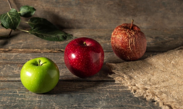 Green red and rotten apples on burlap on wooden boards