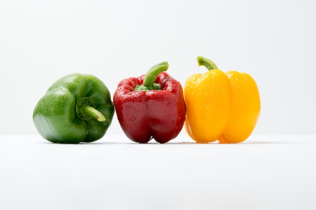 Green, red and yellow bell peppers on white table and white.