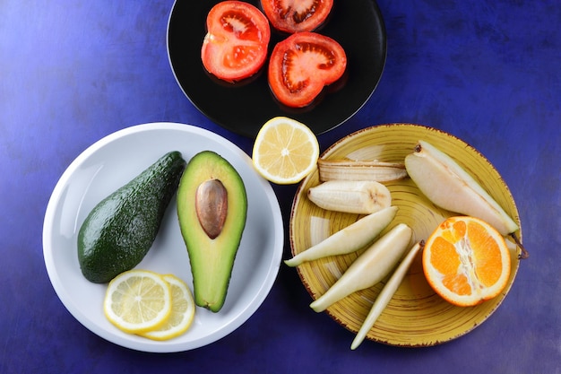 Green red yellow fruits with citruses on a plate on a blue background Vegetarian food concept Closeup food for a healthy snack