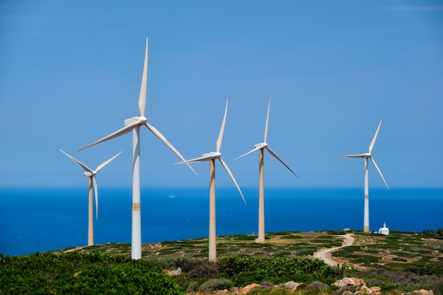 Green renewable alternative energy concept - wind generator turbines generating electricity. Wind farm on Crete island, Greece with small white church