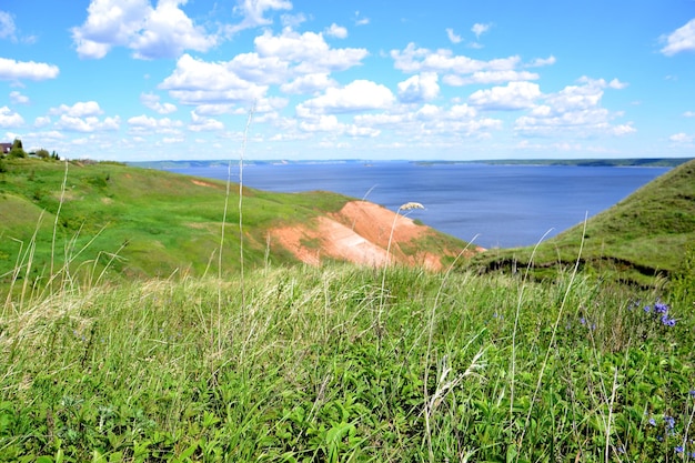 green rolling hills with blue river and sky with clouds on background in sunny day