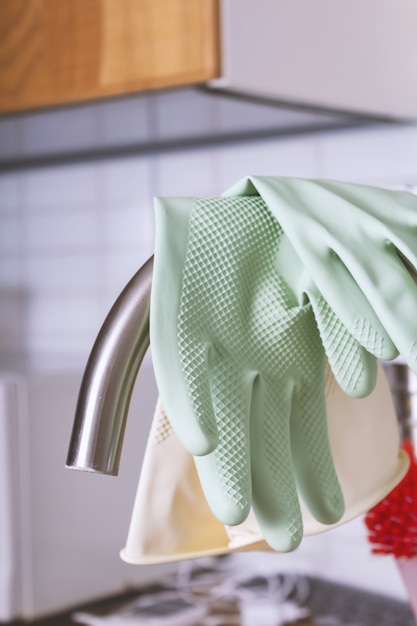 Green rubber gloves hanging on steel faucet