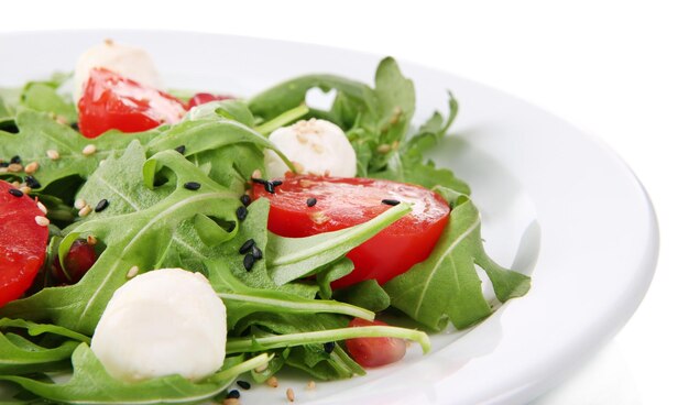 Green salad made with arugula tomatoes cheese mozzarella balls and sesame on plate isolated on white